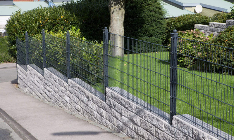 Gestufter Gartenzaun aus Metall als Doppelstabmattenzaun, an einem abfallenden Hang entlang der Straße zur Abgrenzung des Gartens.