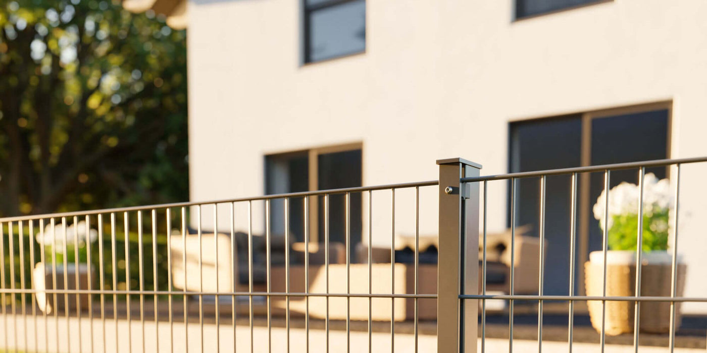 Ein Doppelstabmattenzaun in Anthrazit mit Zaunpfosten mit Abdeckleiste vor einem Neubau Haus. 