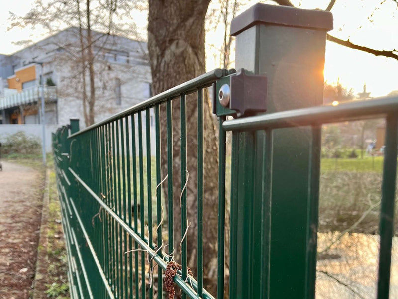 Nahaufnahme eines Gartenzauns aus Metall mit schwarzer Abdeckkappe auf den Pfosten und Edelstahl-Plättchen als Befestigungspunkte für den Doppelstabmattenzaun.