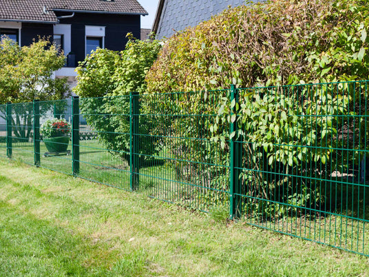 Grüner Gartenzaun aus Metall als Doppelstabmattenzaun, ergänzt durch stabile Zaunpfosten mit Abdeckleiste im Gartenbereich.