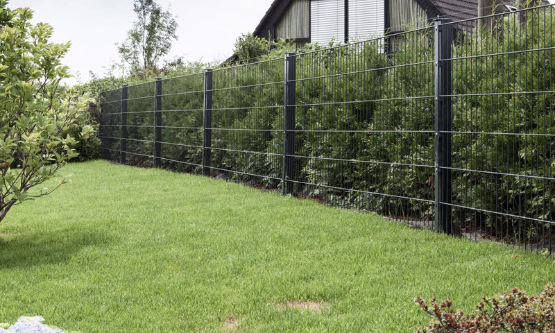 Zaunreihe aus anthrazitfarbenem Gartenzaun aus Metall vor einer dichten Hecke als Gartenabgrenzung.